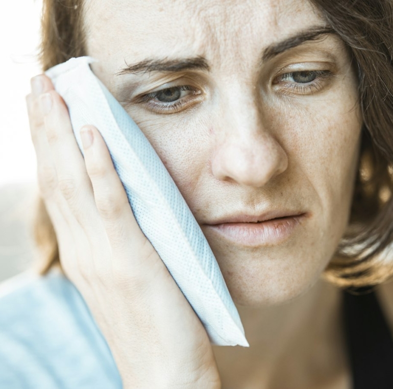 Woman holding an ice pack to her cheek while waiting for an emergency dentist in Muncie, Indiana
