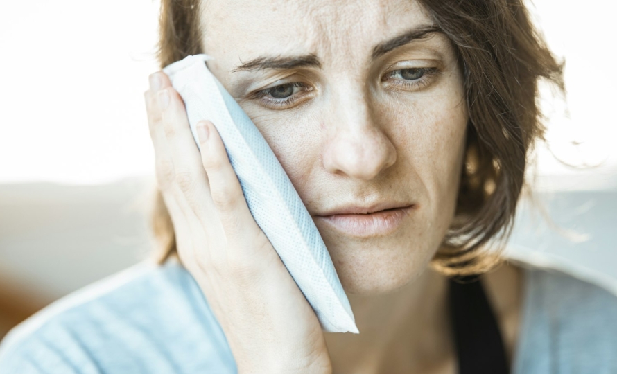 Woman holding an ice pack to her cheek while waiting for an emergency dentist in Muncie, Indiana