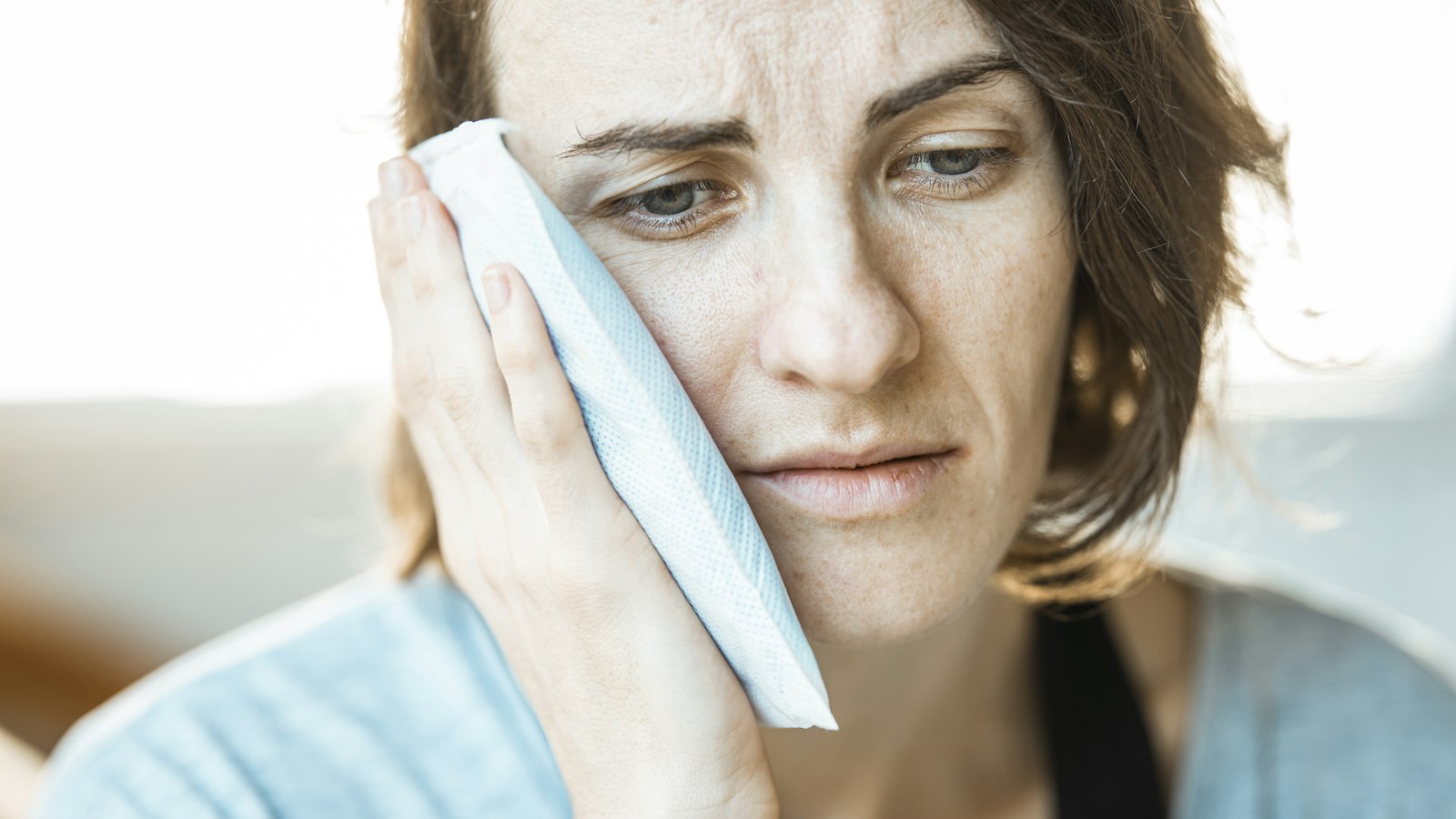 Woman holding an ice pack to her cheek while waiting for an emergency dentist in Muncie, Indiana